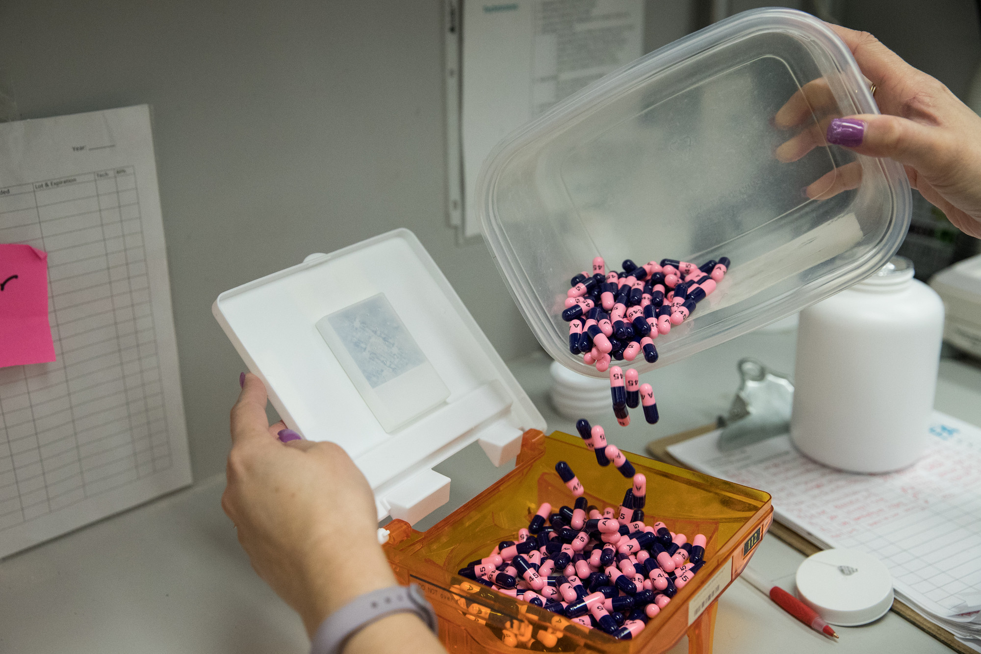 a pair of hands pouring black and pink pills into a box