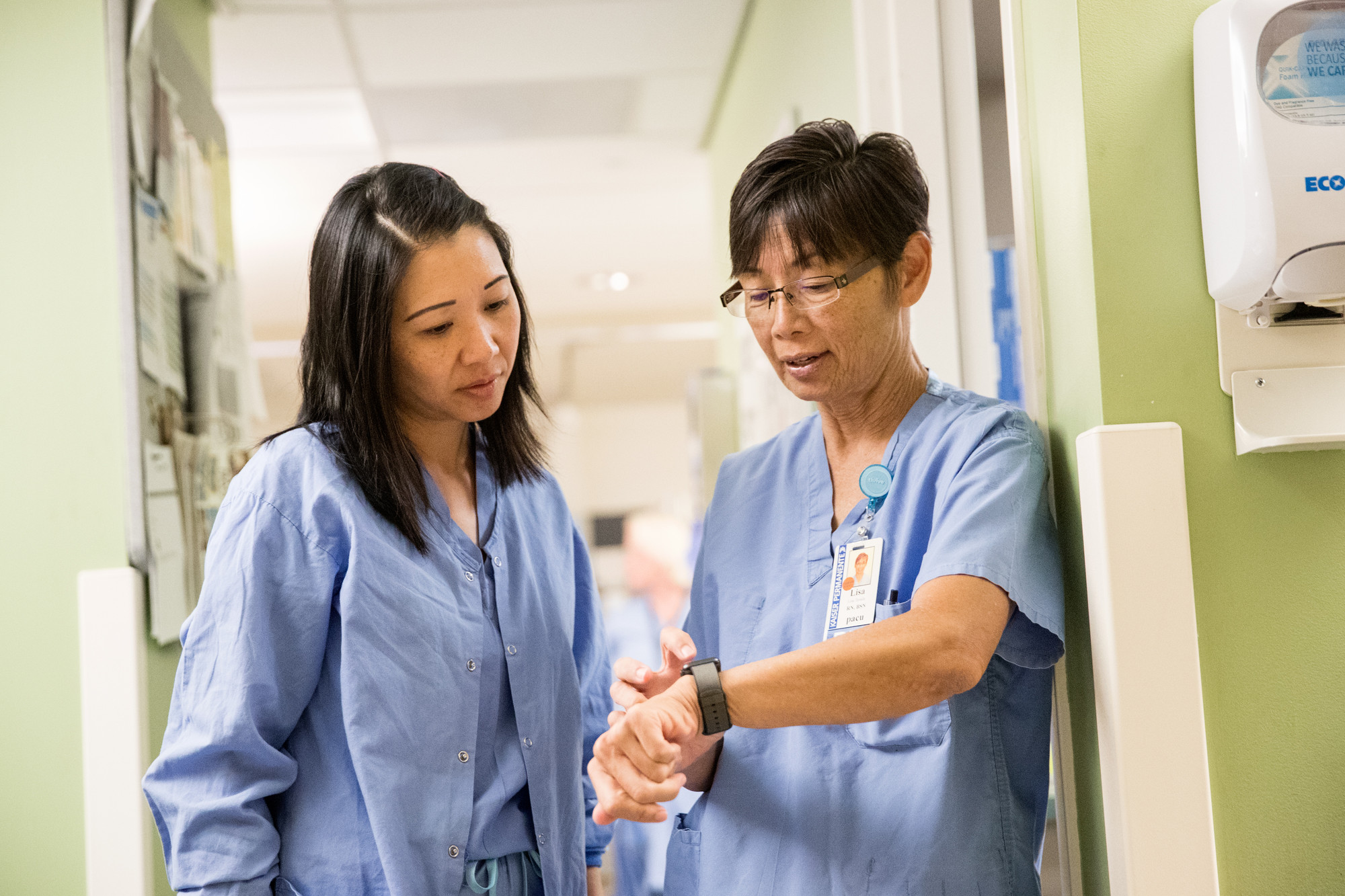 Two nurses, wearing blue scrubs, talking with each other